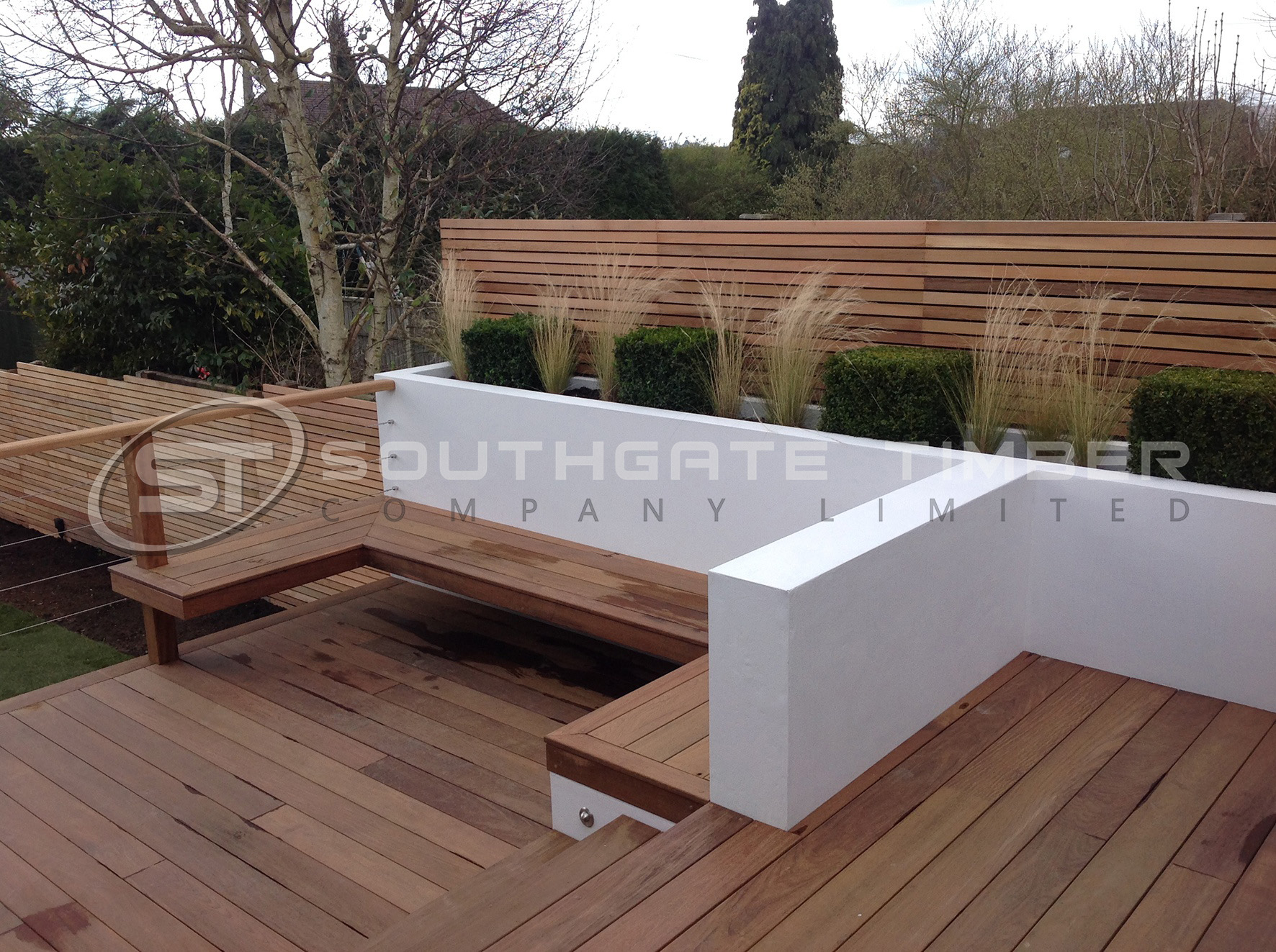 Freshly installed Ipe hardwood decking and built-in seating with a rich brown finish, shown in a modern garden setting. The natural grain and colour of the Ipe boards highlight their premium appearance before any weathering or oiling.