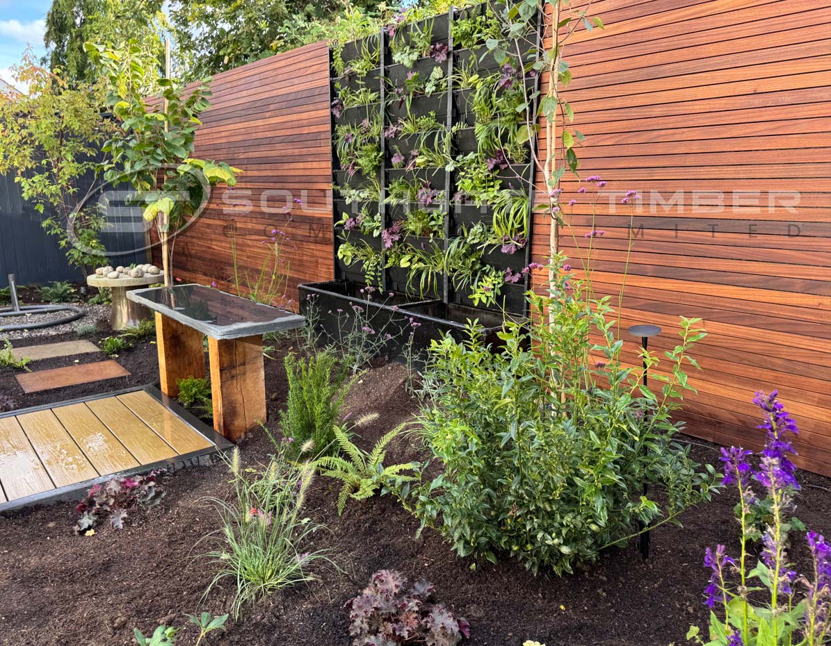 Thermo Ayous horizontal slatted fencing with rich golden-brown tones, used in a landscaped garden with vertical planter wall and modern planting, supplied by Southgate Timber.