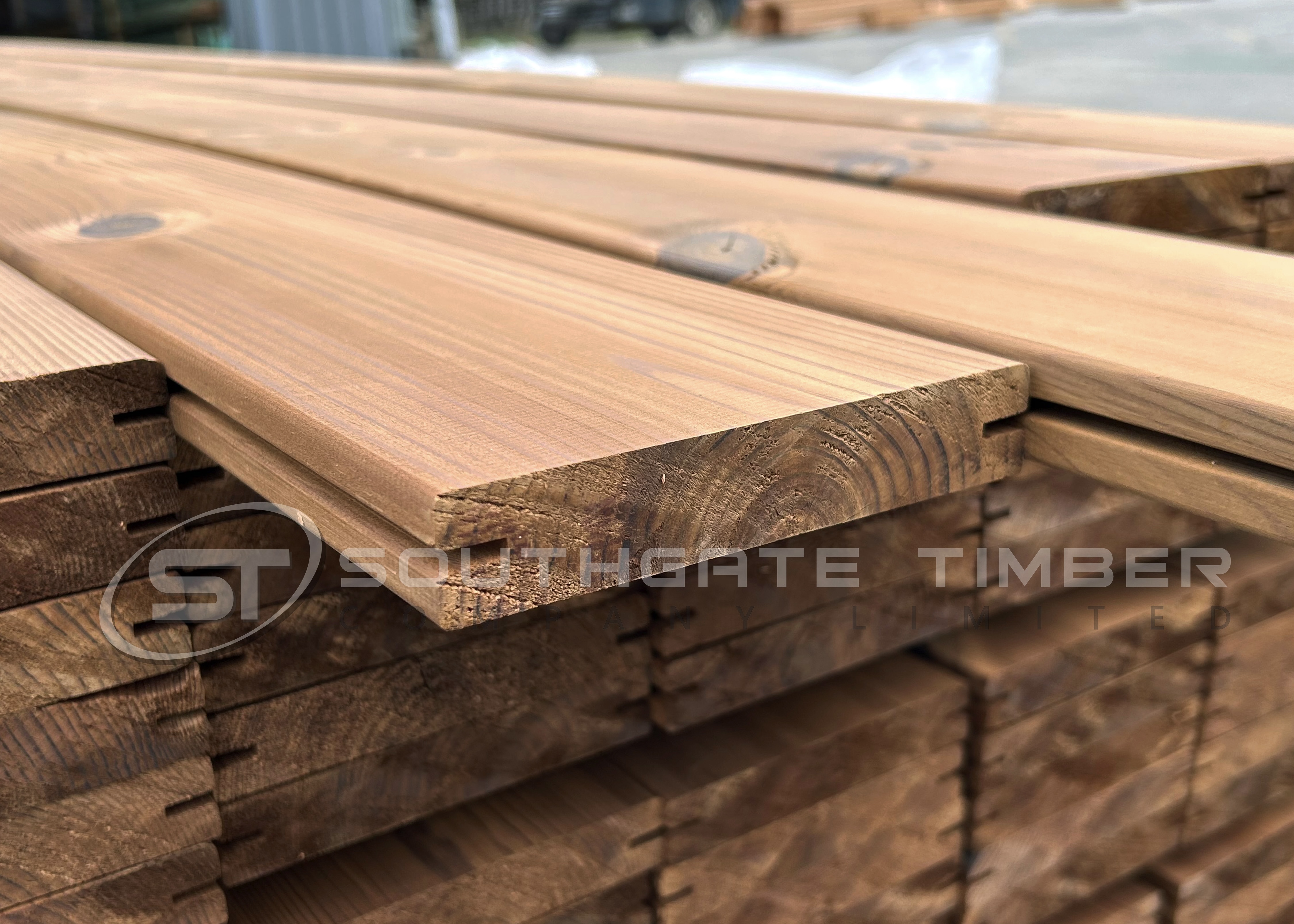 Close-up stack of Thermowood Pine decking boards showing the smooth profile, enhanced grain and tongue-and-groove detail. The heat-treated pine displays its signature warm brown tone, illustrating an affordable, stable and lightweight softwood decking option.