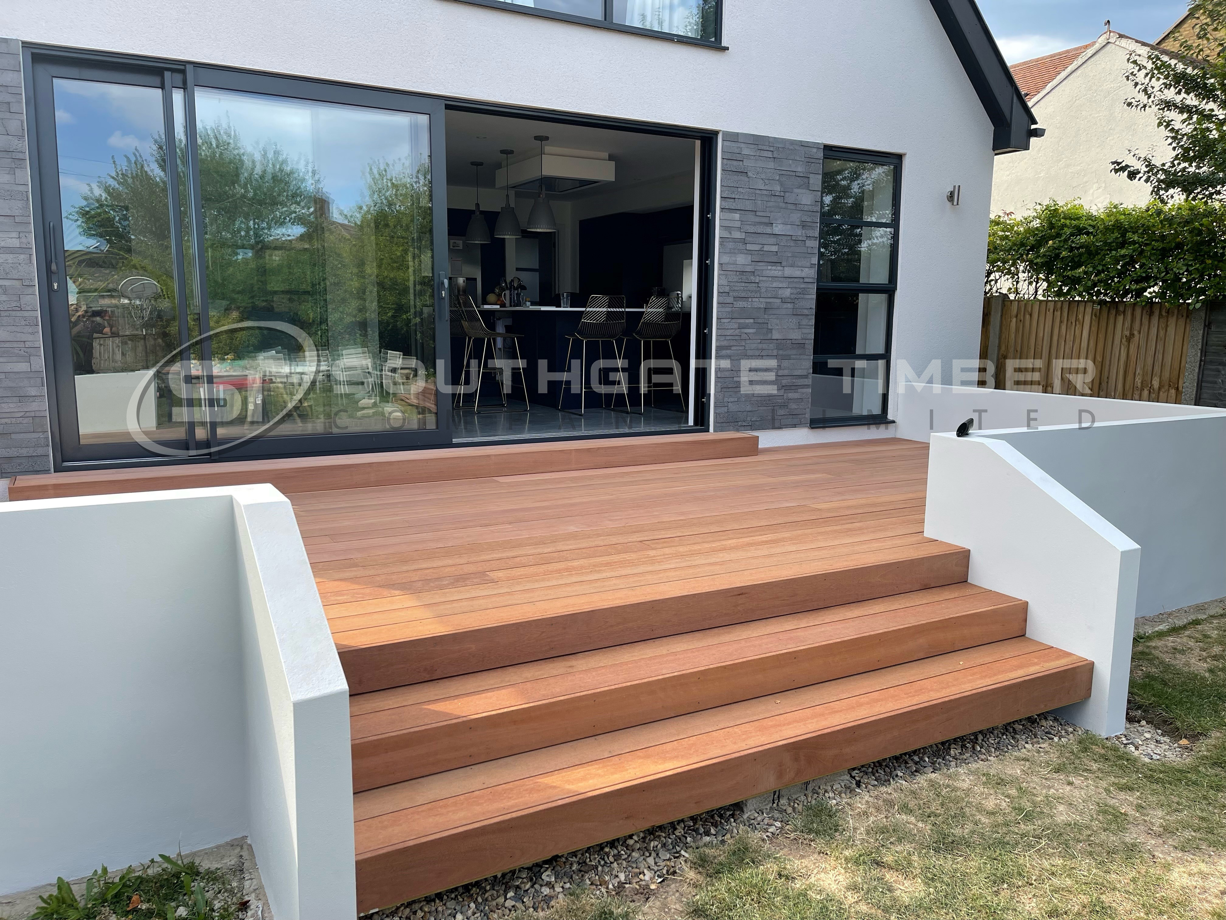 Modern garden patio featuring Yellow Balau smooth-2-sides FSC hardwood decking installed on wide steps leading to sliding doors. The rich golden-brown Balau boards show a clean, premium finish, demonstrating an affordable and durable hardwood decking option.
